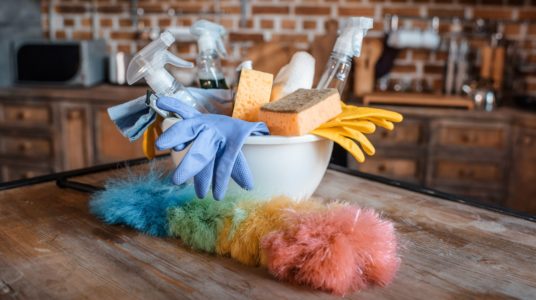 Des gants de nettoyage et un plumeau anti-poussière posés près d'une bassine par une femme de ménage.