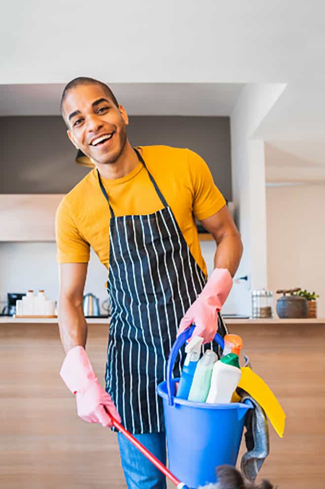 Un jeune agent de ménage à domicile à Genève souriant, nettoyant le sol d’une cuisine.